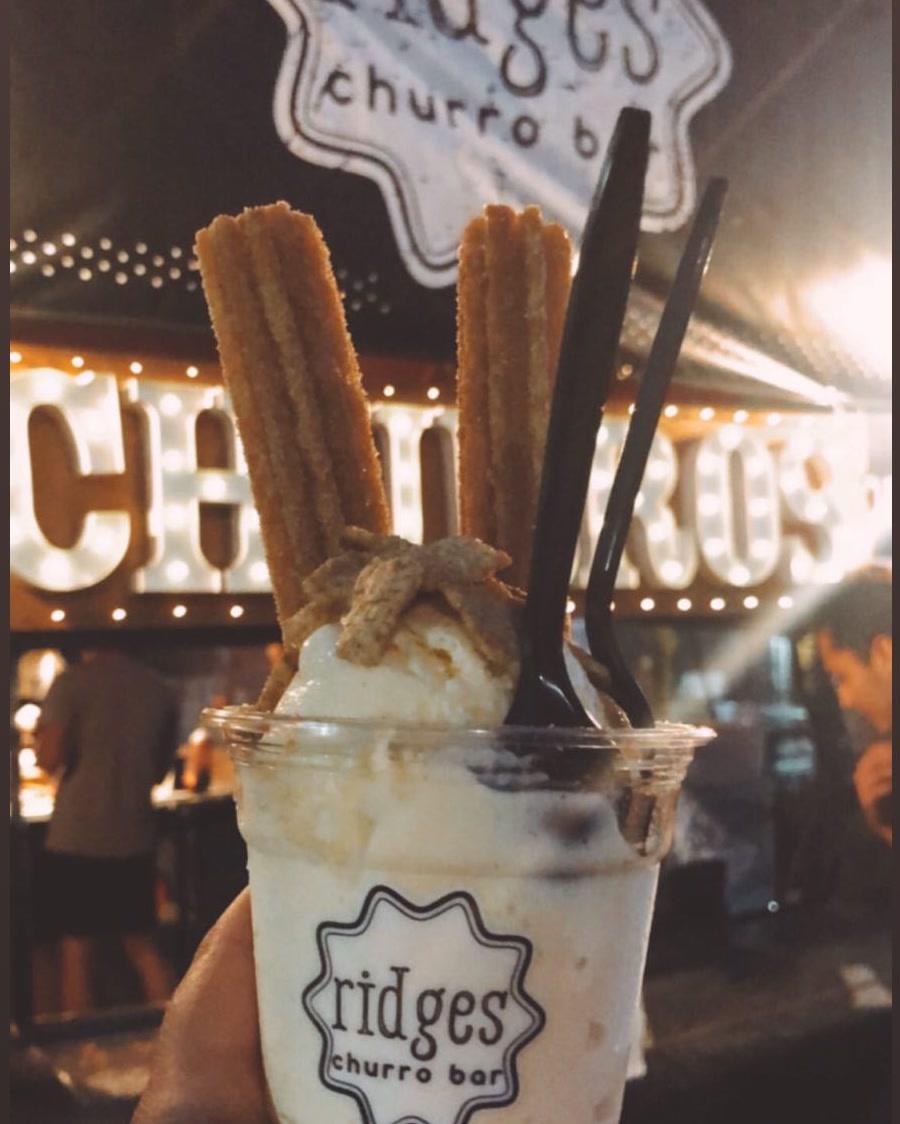 A Ridges churro sundae held in front of the glowing CHURROS marquee at night.